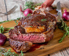 美味的新鲜烤肋骨眼牛排与骨头称为战斧牛排煮中等罕见，与牛排刀和香草在木制切菜板上。爱尔兰优质肉类 
