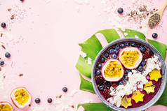 美味的美味的冰沙阿凯碗制作野生浆果, 装饰与切百香果, 椰子片, 和可可豆笔尖粉红色的背景