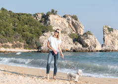年轻的金发女人和狗在海滩边散步很开心