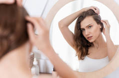 3.年轻女子在家里检查镜子里的头发是否稀疏