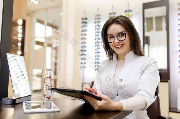 医学、药学和光学。穿着白袍的年轻女医生或药剂师的画像在光学诊所里写下<strong>菜谱</strong>.
