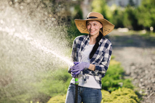 美丽的年轻园丁妇女在炎热的夏天的时候一边给花园浇水, 一边享受乐趣.