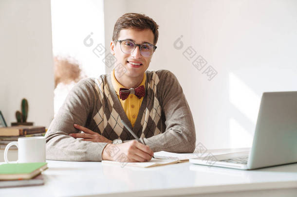 一个快乐的、积极向上的年轻人坐在桌旁，在屋里写作业，研究相机的画像.