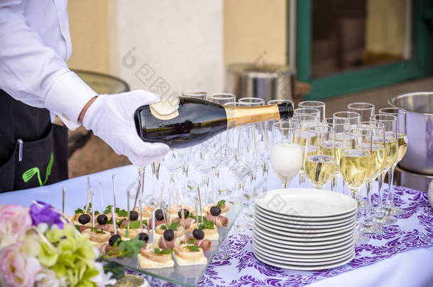 侍者的手在酒杯倒白葡萄酒或香槟。把酒倒进眼镜的明亮画面.