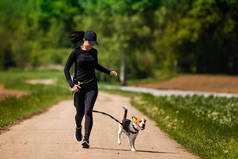 运动女孩带着一条狗（小猎犬）在乡间公路上跑步，并带着摄像机。