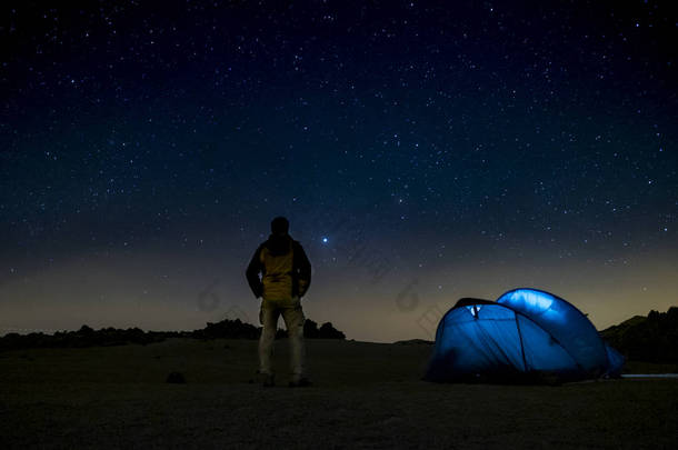 夜间拍摄，背景是深蓝色的天空和星星- -旅行和自由的概念，帐篷在野外野外<strong>野营</strong>- -站着观看周围的风景