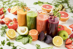 新鲜挤榨的果汁、水果和蔬菜，放在用水果装饰的白色桌子上的玻璃杯中