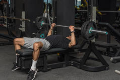 运动的年轻拉丁男子在健身房提起杠铃。体操胸肌运动。有选择的重点