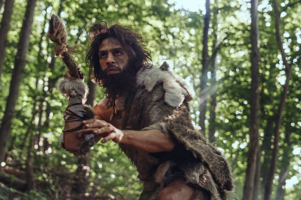 史前森林中头戴兽皮、头戴石钉猎杀的原始人的肖像。史前尼安德特人猎人准备向丛林里扔长矛