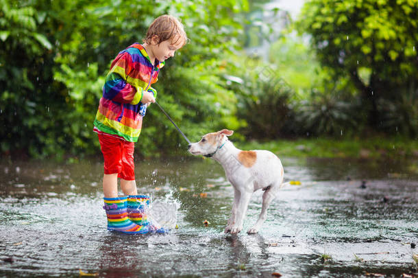 孩子和狗在秋天公园的雨中玩耍.小孩走狗。<strong>下雨天</strong>,小男孩在泥泞的水坑里跳跃.雨靴和夹克，户外穿着。儿童防水鞋和外套.