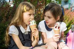 两个女学生的肖像7岁的学校校服与背包吃冰淇淋。背景城市, 夏天, 人行道, 装饰灌木.