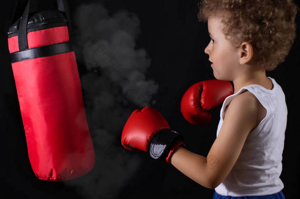 一个戴着红色拳击手套的小男孩乘火车去打拳击袋。 运动、儿童拳击.