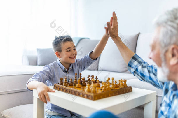 快乐的小男孩在家里和年长的人下棋。与祖父和孙子的家庭关系。<strong>爷爷</strong>和男孙子玩棋盘游戏