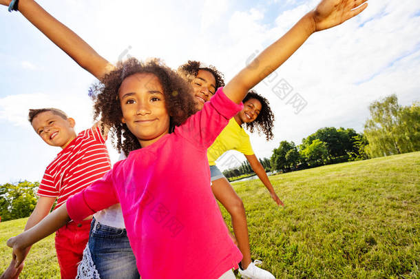 一群快乐的孩子们，有着卷曲的黑人女孩站在他们的前边，展示着张开的手和微笑