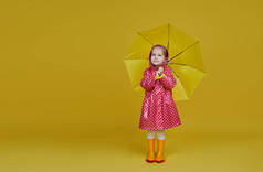 快乐的小女孩，带着黄色的雨伞，红色的雨衣，背景是黄色的。 文本的复制空间