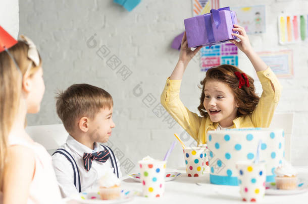 快乐的孩子拿着<strong>礼物</strong>, 而坐在桌子上与<strong>朋友</strong>在生日聚会庆祝活动