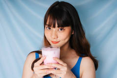 年轻快乐的亚洲黑发女子，双手捧着粉红奶昔.