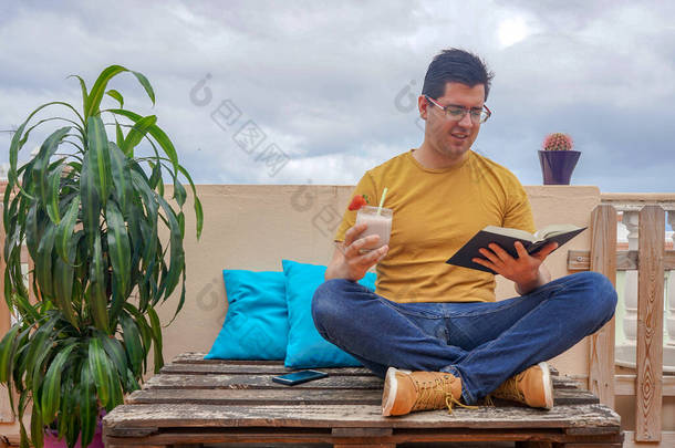 男人在他房子的阳台上看书。他在喝草莓汁.