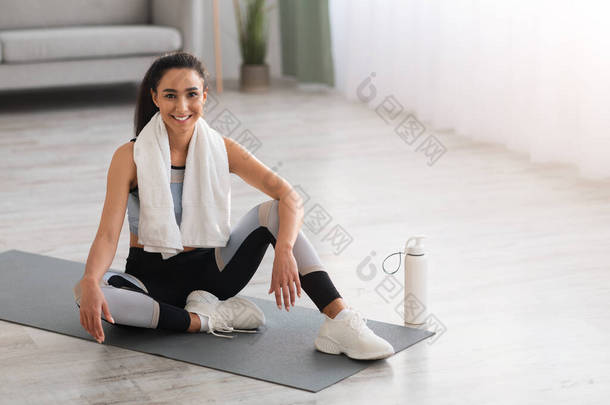 迷人的女士穿着运动服坐在瑜伽垫上休息