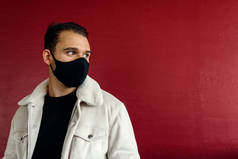 一个戴着黑色面具的年轻人，回头望着街道上的红墙背景。青春、时尚和验尸官的概念带有版权保护的图像.