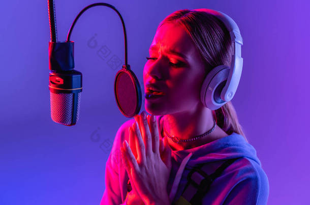 穿着无线耳机的年轻女子一边唱歌一边用紫色滤色器唱歌 