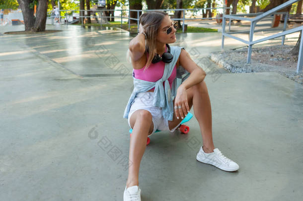 穿着夏装的时髦年轻女子坐在滑板上，坐在滑板上
