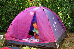 男孩看着一个紫色的帐篷, 而露营, 这是设置直接在绿色