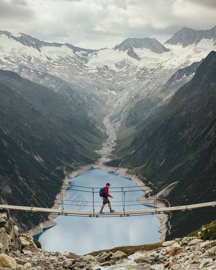 男人背着背包在山上旅行。一位年轻的运动员站在一座悬索桥上，背靠一座山和一座冰川。旅行和积极生活的概念。历险之旅.