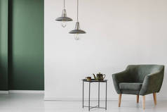 软垫, 深色扶手椅和一个工业边表与茶壶和杯子在一个简约的客厅内饰与绿色的角落