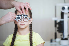 眼科医生为一名穿着黄色T恤、有辫子的少女测试眼镜框的眼科检查.