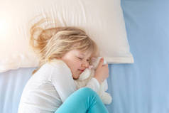 可爱的高加索金发小女孩躺在床上的白色枕头上，睡觉时在房间里睡觉的小宝宝侧面肖像。从上面俯瞰。复制空间案文
