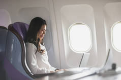 亚洲女青年在飞行、旅行和商务概念中，坐在头等舱靠窗的座位上，使用笔记本电脑