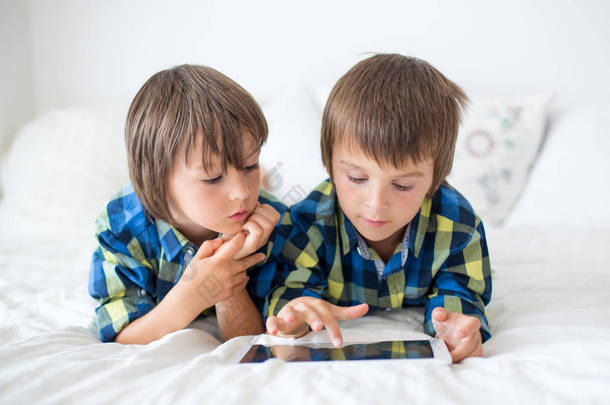 两个学龄前儿童，男孩兄弟在家里躺在床上在平板电脑上玩