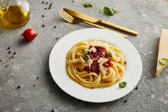 配料附近的白盘上有番茄酱和番茄酱的意大利面食和灰色背景的餐具