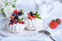 精致的白色蛋白甜饼与新鲜的浆果在盘子里。甜点帕夫洛娃特写。白色背景。喜庆的婚礼蛋糕.