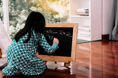 一个6岁的女孩正在她家的小黑板上练习数学扫帚，她正在度假、构思和教育