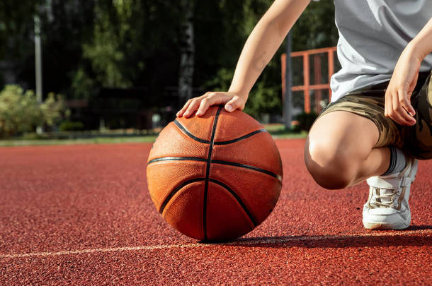 男孩手里拿着一个<strong>篮球</strong>特写镜头，背景是<strong>篮球</strong>场。运动生活方式的概念，训练，运动，休闲，度假.