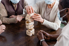 戴着医疗面具的多文化养恤金领取者在家里玩塔木块游戏