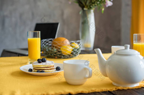 在桌上放上黄色桌布的煎饼、茶杯和果汁杯的特写图