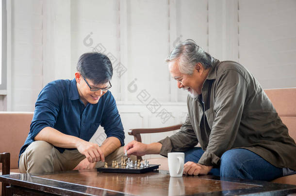 年长的亚洲父亲和中年儿子在客厅下棋，快乐的亚洲家庭<strong>观念</strong>