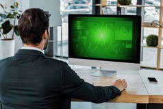 在工作场所的商人的后面视图与计算机屏幕与图在办公室里
