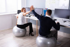 商务人士和女商人坐在健身球给高五个办公室