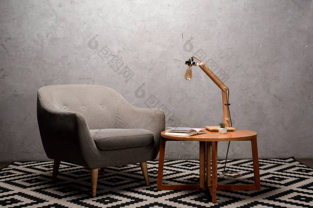 客厅的内部，靠近木制桌子的舒适的灰色现代扶手椅和地毯上的灯
