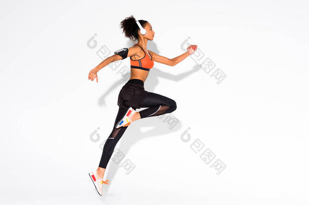 在耳机和智能手机袖标跳在白色美丽的运动非洲裔美国女运动员的侧视图