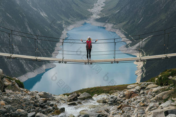 带着背包在山上旅行的女孩。一个年轻的女孩站在一座悬索桥上，在高山和冰川的背景下。旅行和积极生活的概念。欧洲的冒险之旅.