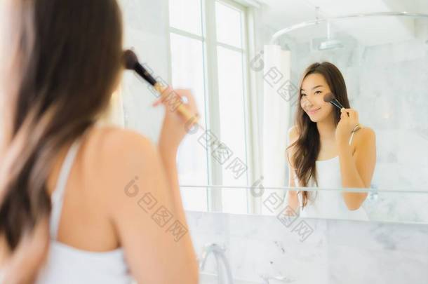在浴室的镜子里，美丽的年轻亚洲女人在镜子前温习和化妆