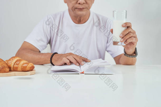 老人在吃早餐时喝牛奶和看书