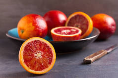 血或红色橘子在蓝色碗和刀在灰色的背景。新鲜成熟的柑橘类水果。选择健康的素食、排毒或饮食概念