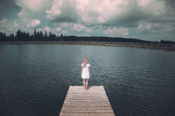 穿着白色衣服的金发碧眼的女人站在湖边的木码头上。使用的色调<strong>滤镜</strong>效果. 