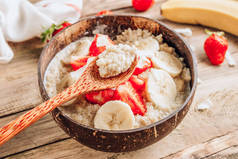 昆诺阿粥与椰奶和新鲜草莓在椰子碗木制乡村背景。健康乳糖和无麸质早餐。有选择的重点
